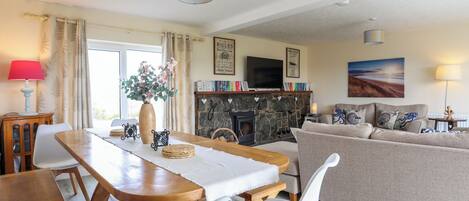Una sala de estar acogedora con una mesa de comedor de madera, sillas blancas, un sofá beige y una chimenea de piedra.