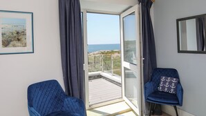 Ett rum med utsikt över havet, en inramad tavla på väggen och två blå stolar.