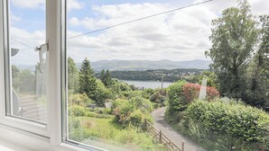 A view from a window overlooking a lush garden with a pathway, a wooden fence, and a distant lake with mountains in the background. - Ty Mawr (Menai Bridge)