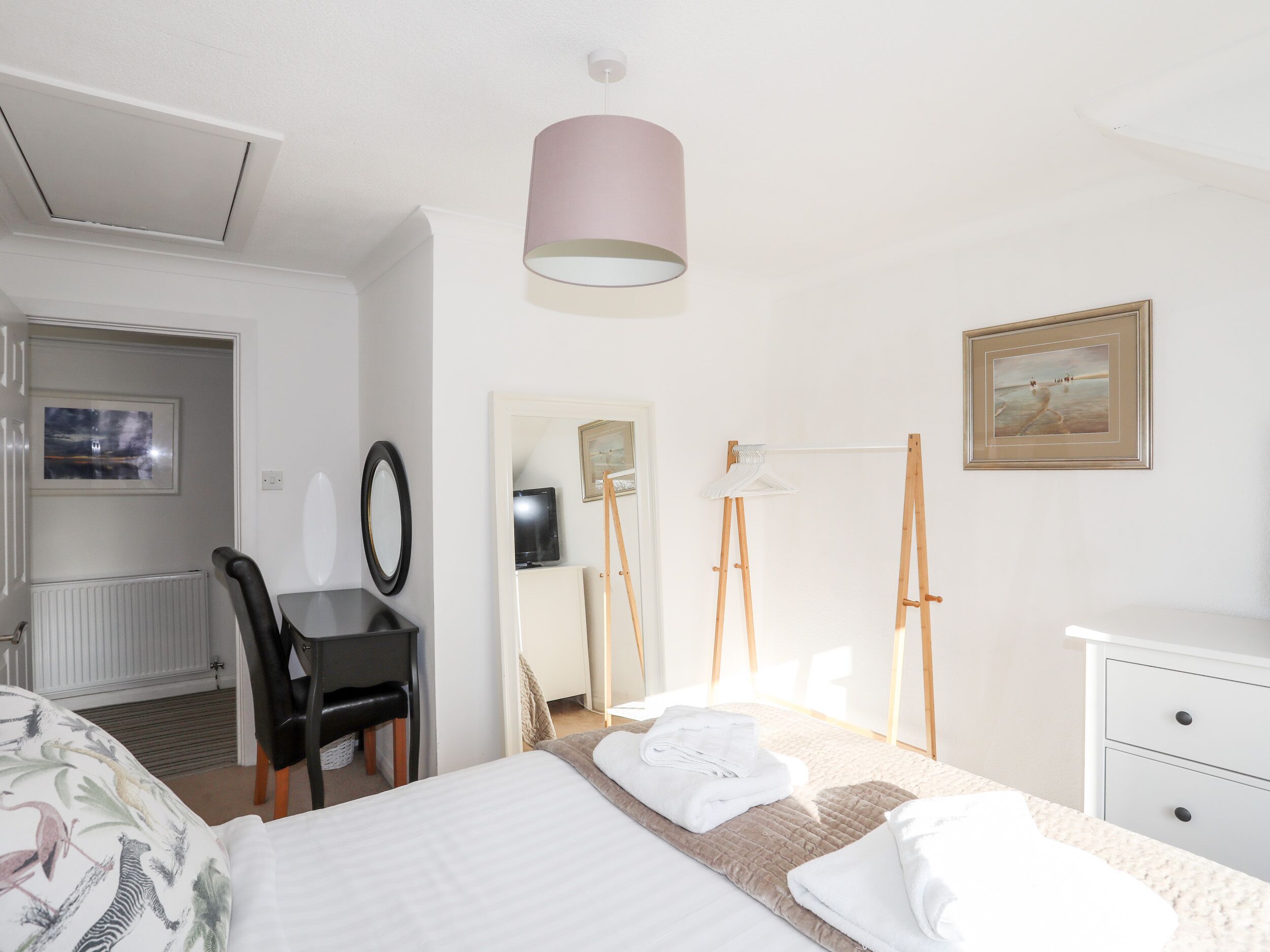Una habitació d'hotel amb un llit, una taula de treball, una cadira, un mirall, un cavallet i un quadre a la paret.