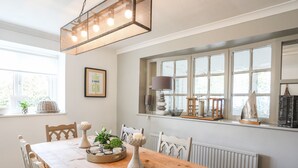 A dining area with a wooden table, chairs, a chandelier, and a window with a view. - Ty Mawr (Menai Bridge)