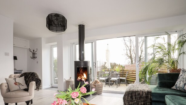 A modern living room with a fireplace, a dining area, and a green sofa. - Ty Mawr (Menai Bridge)