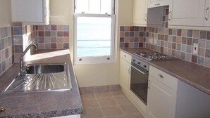 A compact kitchen with a window, a sink, a stove, and cabinets.