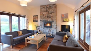 Ein Wohnzimmer mit Kamin aus Stein, zwei Sofas, einem Couchtisch und einem Fernseher.