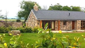 Ein Steinhäuschen mit dunklem Dach, Schornstein und einer Veranda mit Holztüren.