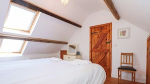 A bedroom with a large bed, wooden beams, a wooden door, and a small chair. - Hafod (Caernarfon)