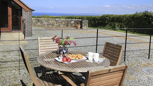 A patio with a round table, two wooden chairs, a vase with flowers, a plate of cookies, and two white cups. - Hafod (Caernarfon)