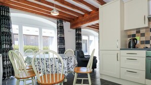 A kitchen with white cabinets, a black countertop, and a coffee maker. There is a dining area with a table and chairs, and a view of the outside through large windows. - Hafod (Caernarfon)