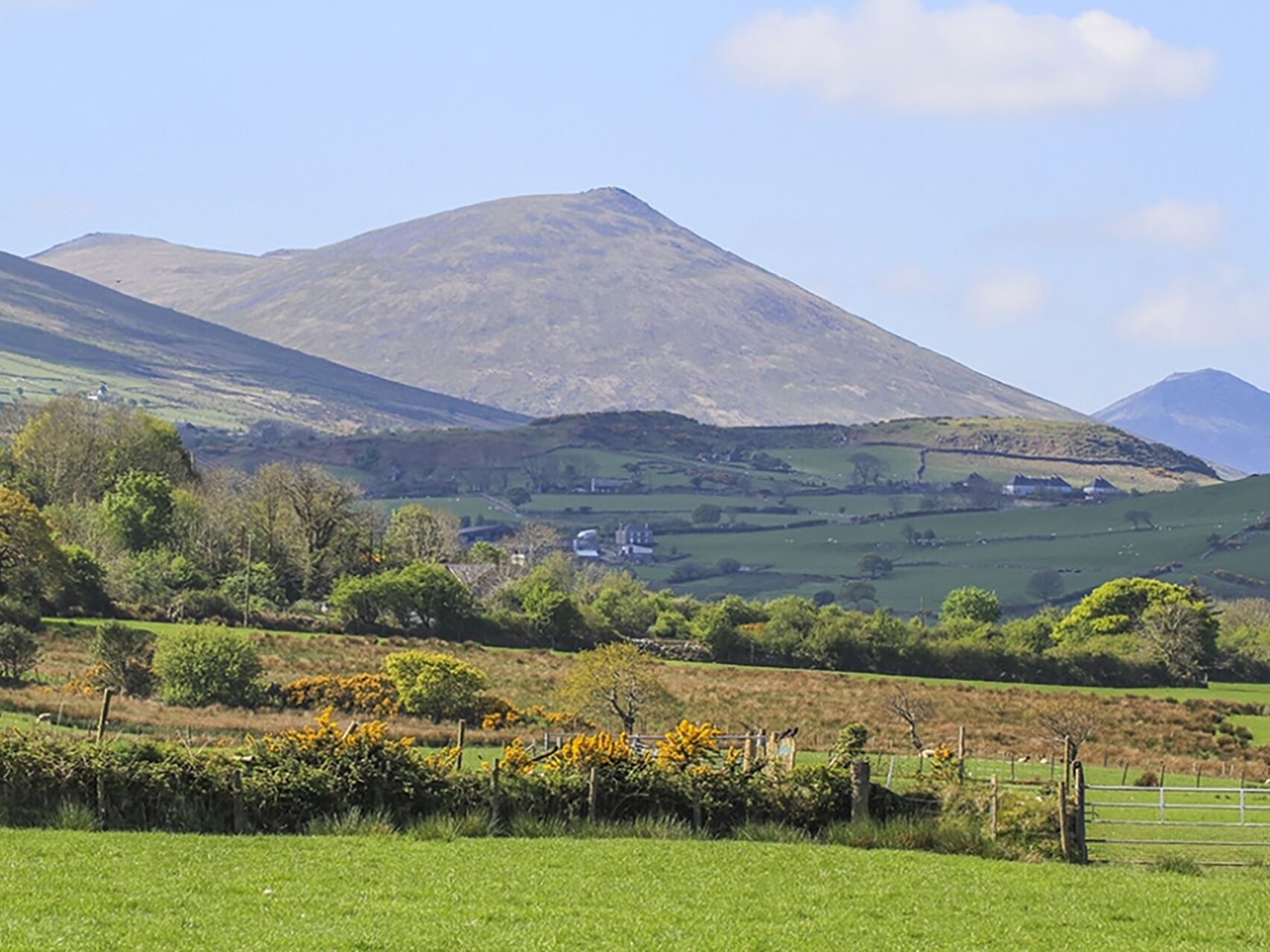A rural landscape with rolling hills, a mountain in the background, and a fence in the foreground.