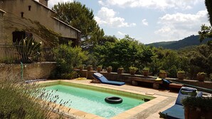 A swimming pool with lounge chairs, surrounded by potted plants and a stone wall.