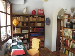 Une pièce comprenant une grande bibliothèque remplie de livres, un bureau avec des papiers et une chaise, ainsi qu’une fenêtre avec des rideaux.