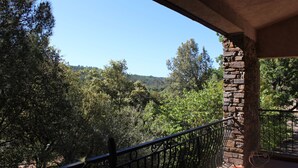 A balcony with a stone pillar, a metal railing, and a view of a forested hillside.