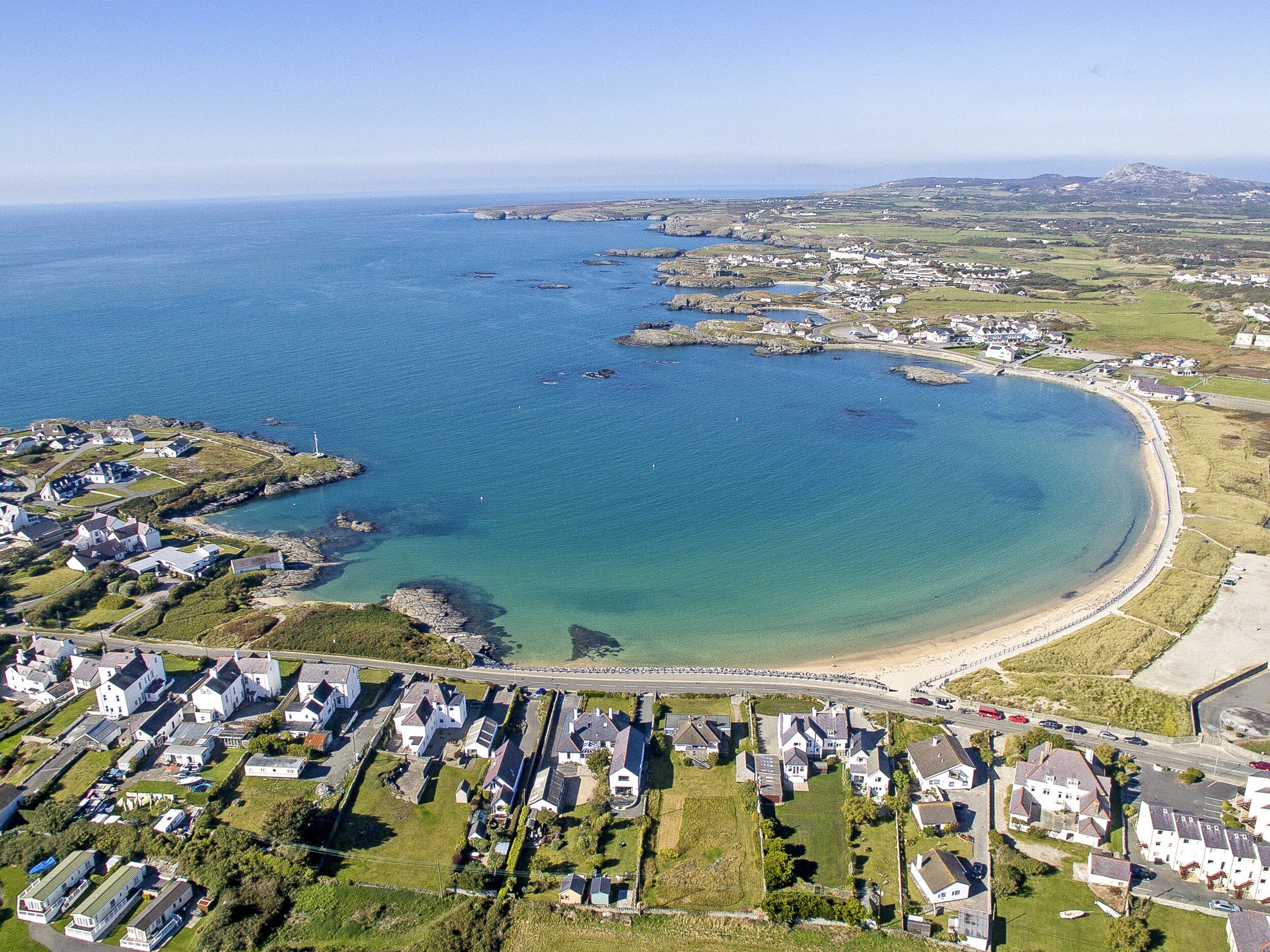 An aerial view of a coastal residential area with houses, a beach, and a clear blue sea.
