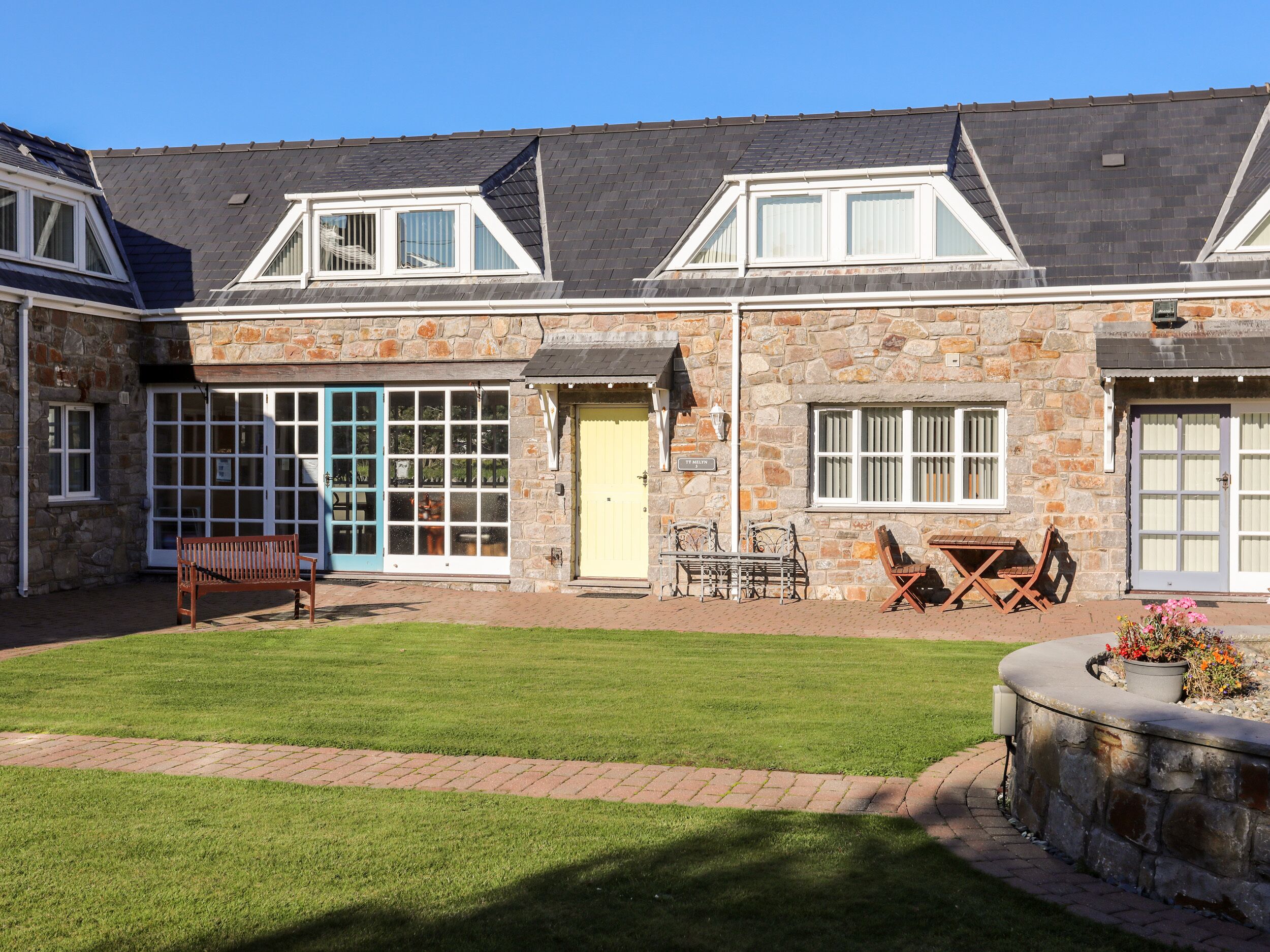 A stone building with a well-maintained lawn, outdoor seating area, and a stone wall with flowers.