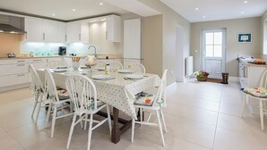 A modern kitchen with white cabinetry, a dining table set for six, and a small island with a sink. - West View (Rhosneigr)
