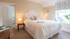 A bedroom with a large bed, a bedside table, a chair, and a window with a view. - West View (Rhosneigr)