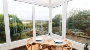 A conservatory with a table set for two, large windows, and a view of the garden.