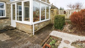 A stone house with a conservatory featuring glass doors and a white frame.