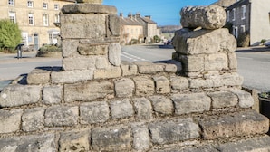 A stone monument with a plaque, set on a cobblestone base in a street with buildings in the background.