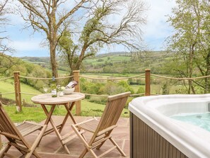 Un bain à remous sur une terrasse, avec une table et deux chaises, offrant une vue imprenable sur la campagne environnante.