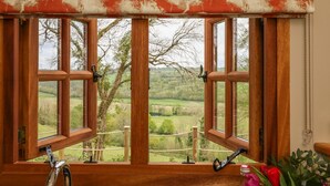 A window with a view of a rural landscape, wooden window frames, and a metal curtain rod.