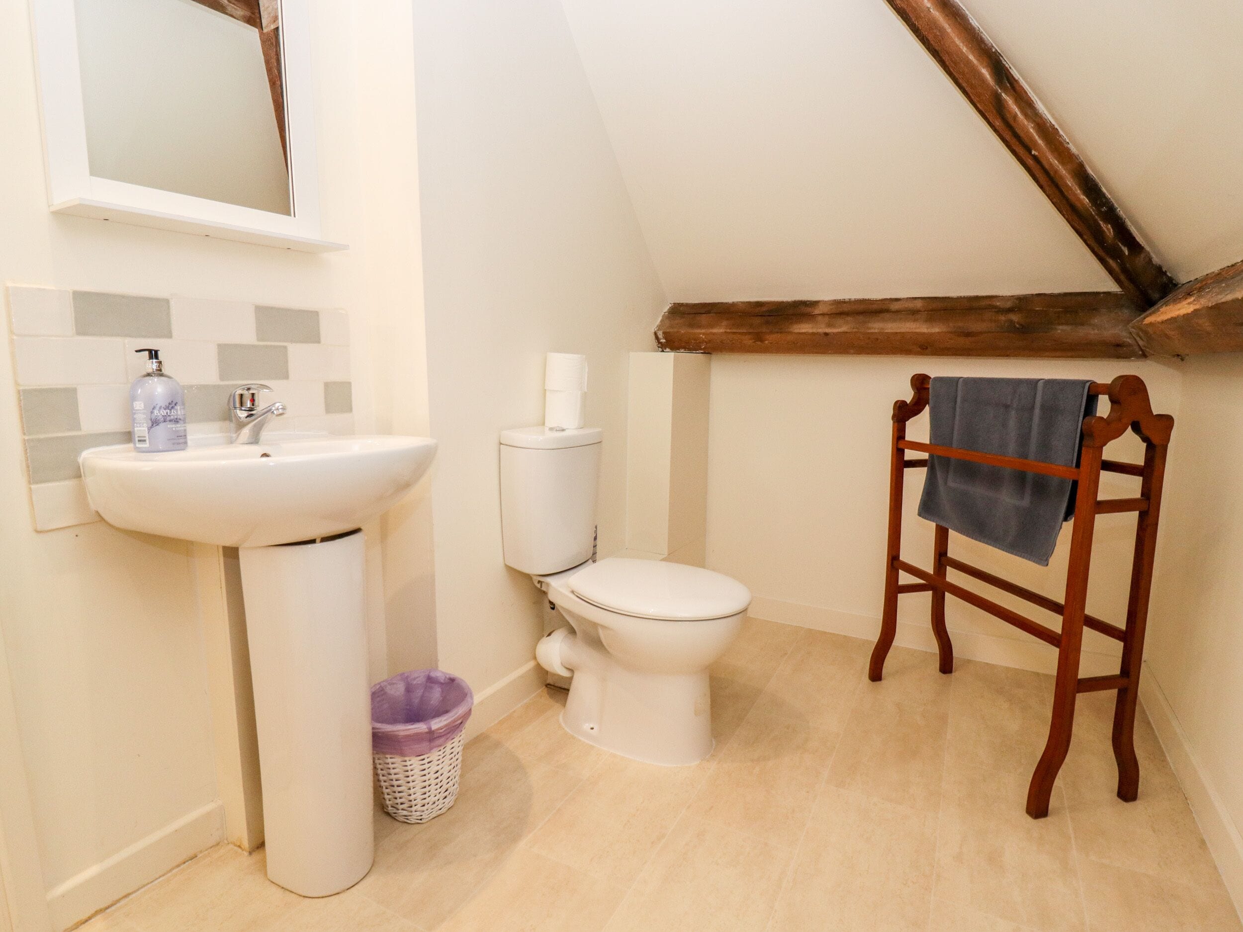 A small, well-lit bathroom with a white sink, toilet, and wooden towel rack.