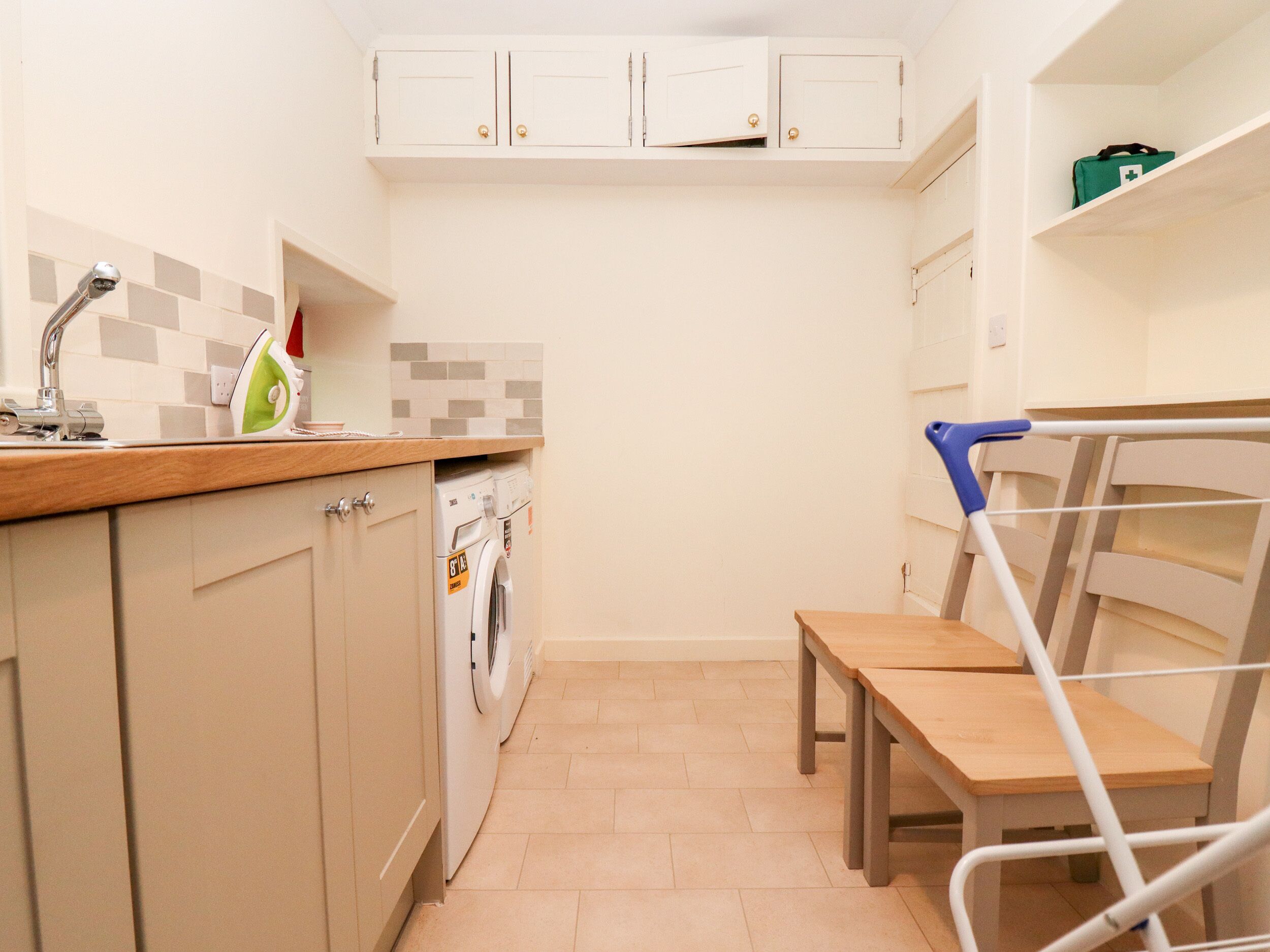 Uma cozinha compacta com máquina de lavar, pia e uma pequena área de refeições com cadeira e mesa.
