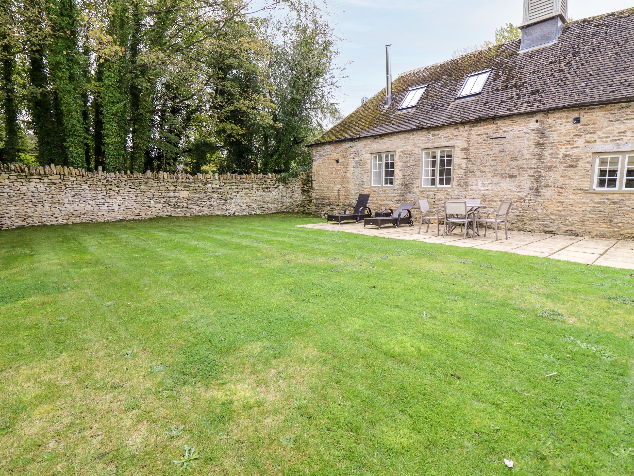 Un bâtiment en pierre avec un mur en pierre, une pelouse et du mobilier d’extérieur.
