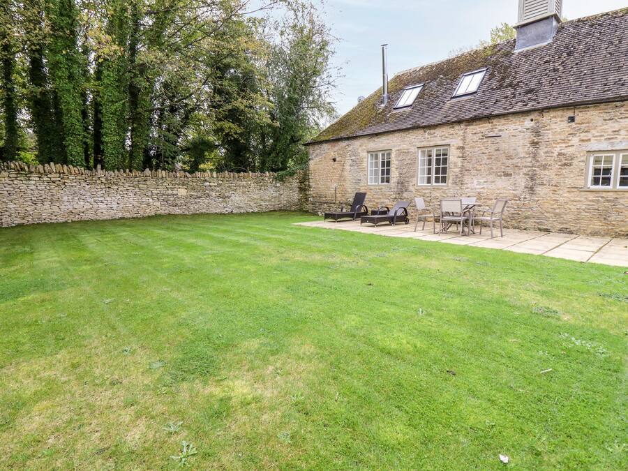 A stone building with a stone wall, a lawn, and outdoor furniture.