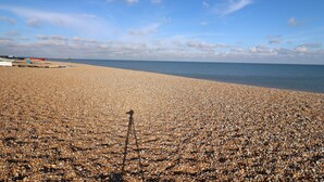 Ein Kiesstrand mit Booten und einer Pier im Hintergrund.