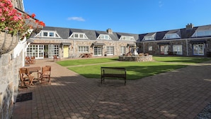 A courtyard with stone buildings, outdoor seating, and a fountain. - Tyn Towyn - Ty Gwyrdd (Holyhead)