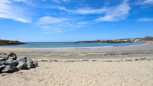 A beach with clear skies, rocky foreground, and distant buildings. - Tyn Towyn - Ty Gwyrdd (Holyhead)