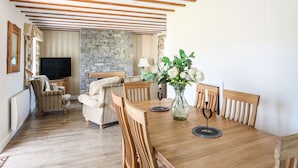 A dining area with a wooden table, chairs, a stone fireplace, and a television in the background. - Tyn Towyn - Ty Gwyrdd (Holyhead)