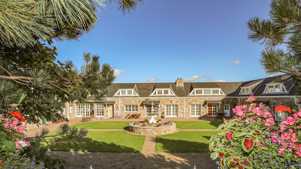 A stone building with a well-maintained lawn and a fountain in the center. - Tyn Towyn - Ty Gwyrdd (Holyhead)