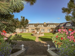 A stone building with a well-maintained lawn and a fountain in the center. - Tyn Towyn - Ty Gwyrdd (Holyhead)