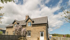 Une maison en pierre avec un toit en pente, une clôture en bois et une table de pique-nique dans la cour.