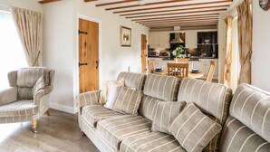 A cozy living room with a striped sofa, a wooden dining table, and a kitchen in the background. - Tyn Towyn - Ty Oren (Holyhead)