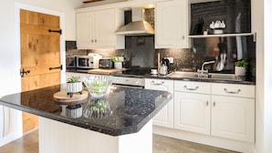 A modern kitchen with white cabinetry, a black countertop, and wooden beams on the ceiling. - Tyn Towyn - Ty Oren (Holyhead)