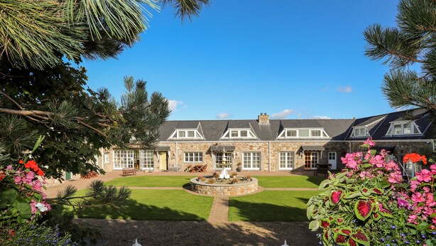 A stone building with a well-maintained lawn and a fountain in the center. - Tyn Towyn - Ty Oren (Holyhead)