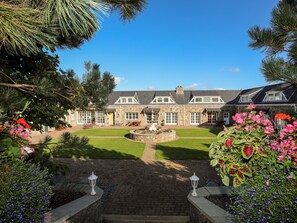 A stone building with a well-maintained lawn and a fountain in the center. - Tyn Towyn - Ty Oren (Holyhead)