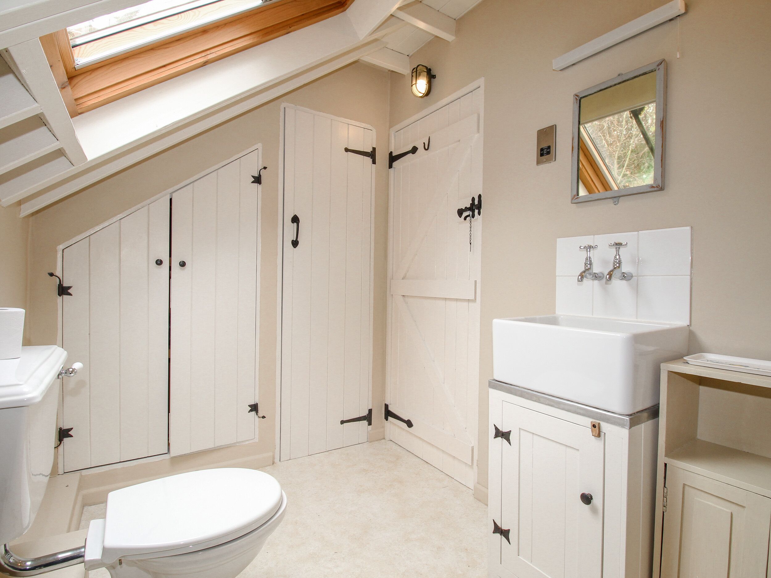 Une salle de bain avec un puits de lumière, des meubles blancs, des toilettes, un lavabo et un miroir.