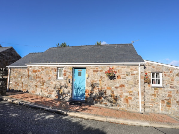 Un bâtiment en pierre avec une porte bleue, une petite fenêtre et une jardinière fixée au mur.