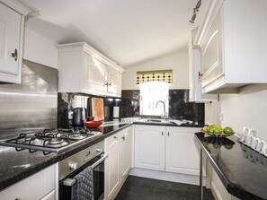 A modern kitchen with white cabinets, a black countertop, and a stainless steel range hood. - Tyn Towyn - Bwthyn Haf (Holyhead)