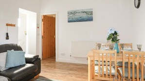 A living room with a leather sofa, a wooden dining table with chairs, a painting on the wall, and a clock. - Tyn Towyn - Bwthyn Haf (Holyhead)
