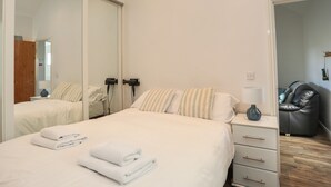 A bedroom with a bed, bedside tables, a mirror, and a chair. - Tyn Towyn - Bwthyn Haf (Holyhead)