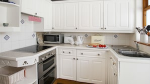 Une cuisine compacte avec des meubles blancs, un four à micro-ondes, un grille-pain et un boîtier à pain.