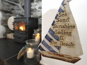 A rustic interior with a wood-burning stove, a candle in a glass jar, and a sailboat decoration. - Gorffwysfa (Holyhead)