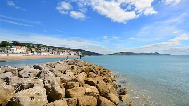 A coastal scene with a rocky breakwater, calm sea, and a row of houses on a hillside. - Valley View Farm Annexe (Lyme Regis)