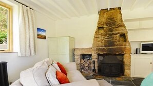 A cozy living room with a stone fireplace, a sofa with cushions, a white cabinet, and a window with curtains. - Valley View Farm Annexe (Lyme Regis)