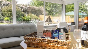 A sunlit room with a grey sofa, a wicker basket on a table, and a view of a garden through large windows. - Clyd Fan (Harlech)